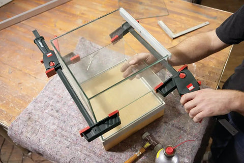 No Sweat One Hand Clamp And Spreader For Tough Woodworking in use, securing glass panels with balanced lever grip.