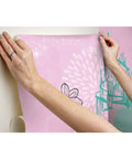 Hands applying Disney Princess Peel And Stick Wallpaper Mural For Kids Rooms, showing floral and castle design on pink and teal vinyl.