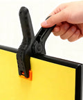 Hand holding Five Pack Four And A Half Inch Spring Clamps For Backdrops And Crafts on yellow board, Heavy Duty Plastic Clips.