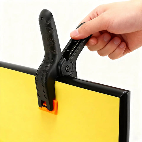 Hand holding Five Pack Four And A Half Inch Spring Clamps For Backdrops And Crafts on yellow board, Heavy Duty Plastic Clips.