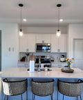 Modern kitchen with island, pendant lights, and wicker stools in a bright, open space.