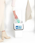 Person placing bottle in trash can with visible Two Pack Recycle Sign Stickers For Trash Cans, Waterproof Fade Resistant Vinyl Labels
