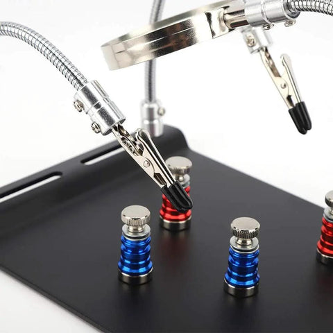 Close-up of Go-To Magnetic Helping Hand with four PCB pillars and two magnifying lamps on a black base for electronics repair.