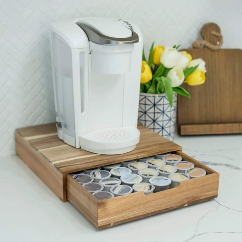Acacia Wood Coffee Pod Drawer Organizer for K Cups and OriginalLine on a counter with a coffee machine and tulips in the background.