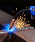 MIG welder gun in action with blue sparks, demonstrating welding on metal; compatible with Miller Multimatic tools.