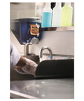 Person washing hands near dispenser labeled with Extreme Weather Sticky Notes 3x3 Inch 45 Sheets Per Pad 3 Pads in kitchen.