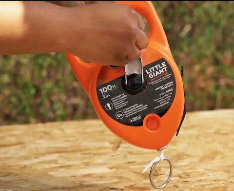 Pro Grade Chalk Line Reel With 110 Foot Reach, 12 Ounce Chalk Capacity, visible on a wooden surface, gloved-hand friendly grip.