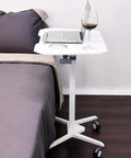 Top Shelf Rolling Laptop Desk With Smooth Moving Casters And Fully Adjustable Height That Tilts Zero To Ninety Degrees For Ultimate Home Office Setup Effortless Studying Or Kick Back Gaming Vibes Anywhere You Park It next to a bed with a laptop and drink.