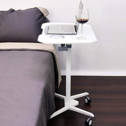 Top Shelf Rolling Laptop Desk With Smooth Moving Casters And Fully Adjustable Height That Tilts Zero To Ninety Degrees For Ultimate Home Office Setup Effortless Studying Or Kick Back Gaming Vibes Anywhere You Park It next to a bed with a laptop and drink.