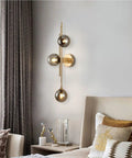 Mid Century Modern Indoor 3 Light Globe Wall Sconce With Smoke Gray Glass Shade And Brushed Brass Finish Vertical Vanity Lamp For Modern Bathrooms Retro Handblown Glass Look Elegant Gold Accents mounted beside a bed in a stylish bedroom.