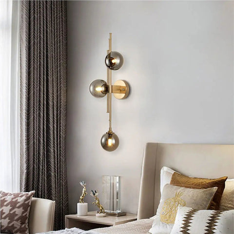 Mid Century Modern Indoor 3 Light Globe Wall Sconce With Smoke Gray Glass Shade And Brushed Brass Finish Vertical Vanity Lamp For Modern Bathrooms Retro Handblown Glass Look Elegant Gold Accents mounted beside a bed in a stylish bedroom.