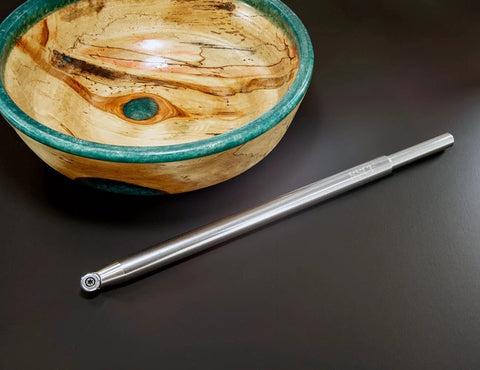 Carbide woodturning tool with long metal handle, for turning acrylic/resin on a wood lathe, shown beside a wooden bowl.