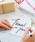 Person writing on 100 Piece Floral Blank Note Cards Set, 4 by 6 Inches, with floral corner, suitable for greeting cards, white background.