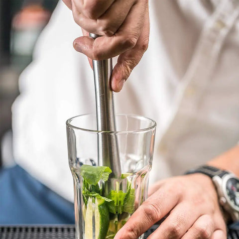 Hand using Food Grade 304 Stainless Steel Cocktail Muddler And Mixing Spoon Set for crushing mint in a glass for mojitos.