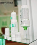 Decorative candles on a mirrored glass surface with a green floral background, featuring embellishments and bows