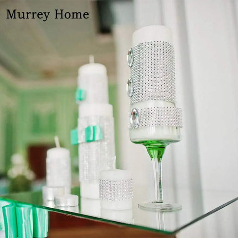 Decorative candles on a mirrored glass surface with a green floral background, featuring embellishments and bows