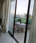 View from inside showing a terrace with a table and chairs, framed by glass sliding doors and sheer curtains.