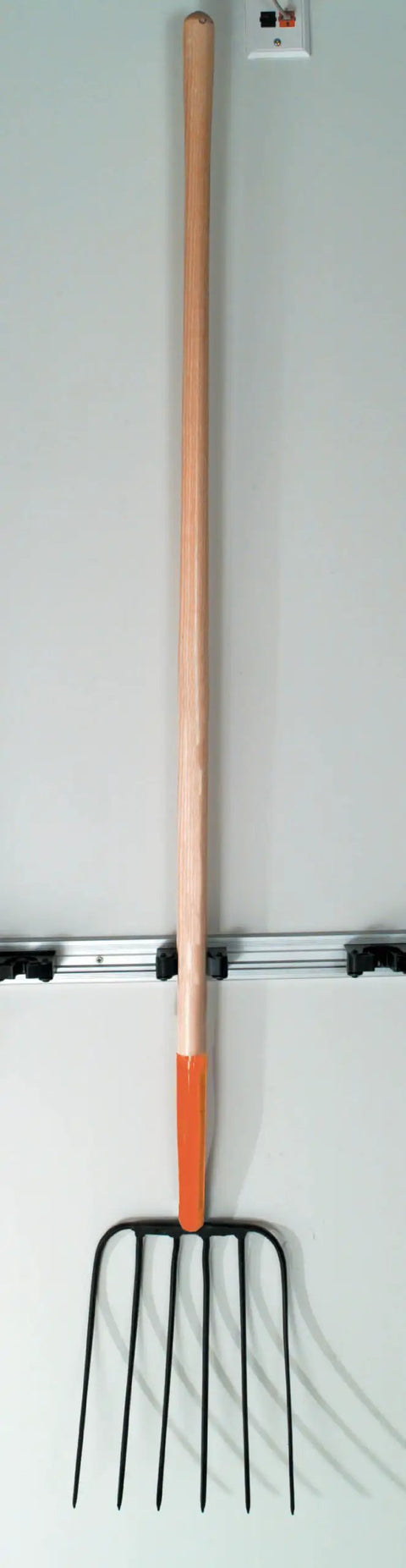 One Piece Forged Steel Manure Fork With Six Scooped Tines And A 54 Inch Ash Handle For Bedding Compost Straw And Farm Cleanup Lightweight Yet Durable Garden Tool against a wall
