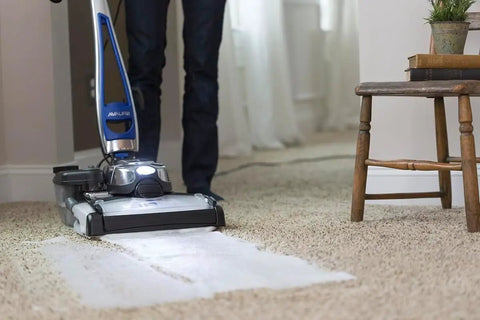 Person using carpet cleaner in living room on light carpet near wooden chair and plant