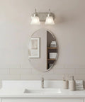 Brushed Nickel 2 Light Vanity Bath Light With Satin Etched Glass Shades above oval mirror in modern bathroom setting, 12.25 Inch Wide, 8 Inch High