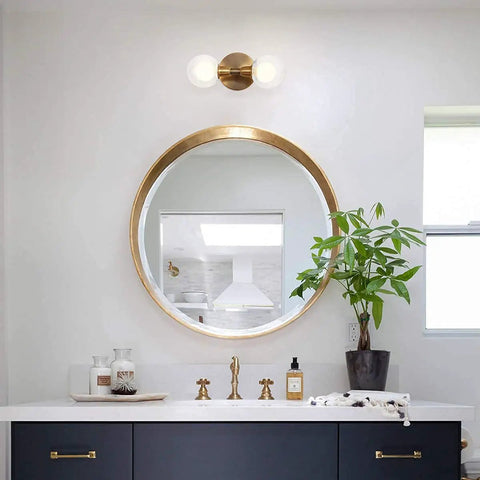 Rock This Mini Two Light Gold Bathroom Vanity Wall Sconce With Clear Glass Shades installed above round mirror in modern bathroom.