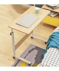 Height Adjustable Mobile Laptop Desk Featuring Smooth Glide Casters And Secure Lock Brakes For Flex Angle Adjustments And Kick Back Living Room Or Home Office Ease placed next to bed on wooden floor.