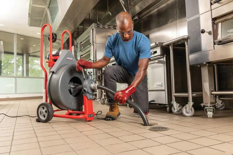 Heavy Workhorse 115 Volt Drain Cleaning Machine With Auto Feed Cable Control and 5 8 Inch Tool Kit used by a contractor in a kitchen setting.