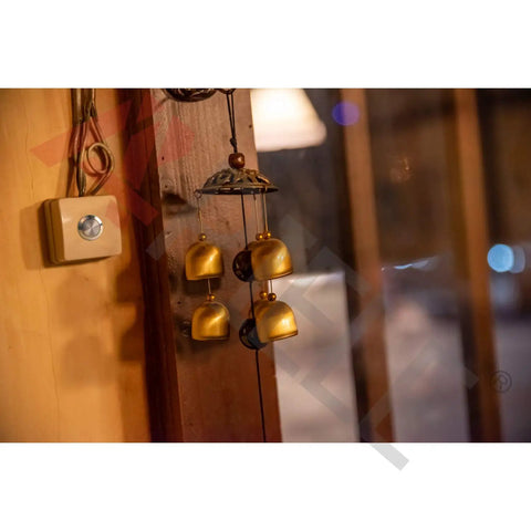 Interior view featuring golden wind chimes hanging near a wooden wall beside a square light switch with a metallic button.
