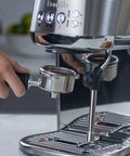 Damson Blue Kickass Espresso Coffee Maker Featuring Auto Milk Frother Quick Heat Technology And Reliable Pressure Pumping For Next Level Barista Quality Home Brews Any Day with a hand holding the portafilter.