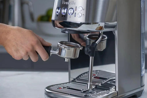 Damson Blue Kickass Espresso Coffee Maker Featuring Auto Milk Frother Quick Heat Technology And Reliable Pressure Pumping For Next Level Barista Quality Home Brews Any Day with a hand holding the portafilter.