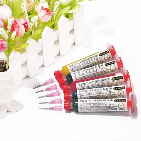Five color UV curable solder kit with needles and plastic tube pistons next to a flower pot for PCB protection solder paste flux