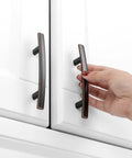 Hand holding Oil Rubbed Bronze Cabinet Pulls 3 Inch 20 Pack, Kitchen Cabinet Hardware, Bronze Drawer Dresser Handles on white cabinet.