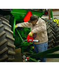 Pro Grade Cordless Grease Gun Workhorse 18 Volt used by a mechanic greasing a tractor in a barn, demonstrating precision and power.