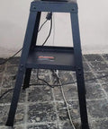 Heavy Duty Steel Bench Grinder Stand Built Like A Tank With Rock Solid Four Leg Base Universal Mounting For Shop Grinders Quick N Easy Setup Glossy Red Frame in black finish with electric cords.