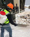 Worker applying Classic Log And Lumber End Sealer Wax Emulsion Water Based Sealant on stacked lumber in snowy yard.