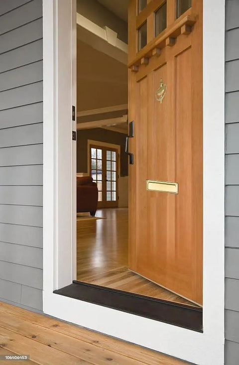 Open wooden door with solid brass mail slot with interior frame, heavy gauge wrought brass construction, polished brass finish.