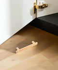 Wooden cabinet pull handle on hardwood floor near open white cabinet with gold hinge and latch detail