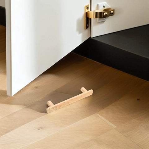 Wooden cabinet pull handle on hardwood floor near open white cabinet with gold hinge and latch detail