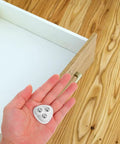 Hand holding white heavy duty peel and stick caster wheels with stainless steel rollers for easy installation.