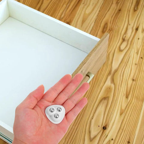 Hand holding white heavy duty peel and stick caster wheels with stainless steel rollers for easy installation.