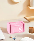 Pink Decor Wooden Desk Calendar Blocks Perpetual Block for Office on a desk with a hand holding a coffee cup