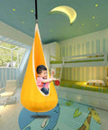 Child playing in Kids Pod Swing Hanging Seat For Indoor And Outdoor Use, Kid Friendly Hammock Chair with 100 Percent Cotton Mat and Cushion, Sensory Swing for Reading and Relaxing, Cozy Hangout That Supports Up To 170 Lbs, Bright Yellow in colorful playroom.