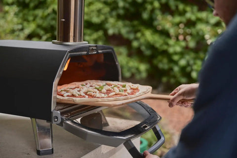 Karu 2 Pro Multi Fuel Pizza Oven For Backyard Grilling Wood Or Gas Fired 16 Inch Stone Pizza Maker with pizza being placed inside.