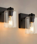 Set Of Two Matte Black Wall Sconces With Clear Glass Shade, Industrial Farmhouse Vanity Lighting Fixtures For Bathroom Mirror And Hallway, shown illuminated on wall