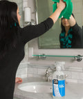 Woman cleaning mirror with Streak Free Glass Cleaner Spray For Windows, Mirrors, Screens And Shower Doors, Removes Fingerprints Dust And Dirt, Unscented Formula, Multi Surface Cleaner, 32 Oz Pack Of 2 visible on sink.