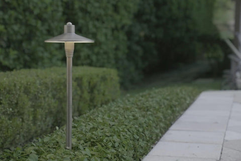 G2 12V Brass Path Light illuminating garden pathway, 24-inch tall, 3W LED, enhancing landscape with warm 2700K glow.