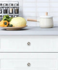 Straight Up Sleek 4 Pack White Marble Cabinet Knobs on modern kitchen drawers with vegetables and utensils in background.