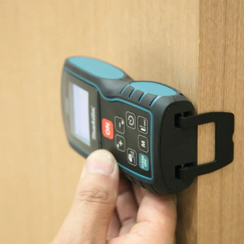 Hand holding Pro Grade Laser Distance Meter With 262 Foot Range And Precision against a wooden surface, showing display and buttons.