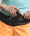 Person placing smartphone into Bounce Free Running Belt For Men And Women, Ultimate Waist Pack With Zip Pockets That Will Not Slip.