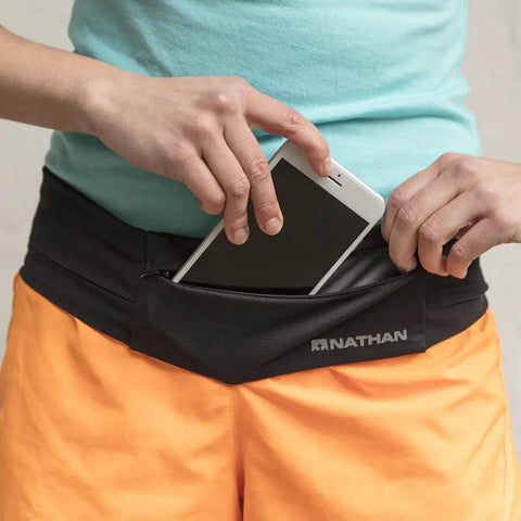 Person placing smartphone into Bounce Free Running Belt For Men And Women, Ultimate Waist Pack With Zip Pockets That Will Not Slip.